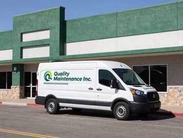 Wide environmental shot of a branded Quality Maintenance Inc. white service van parked outside a clean, modern commercial building in Albuquerque, bright daylight
