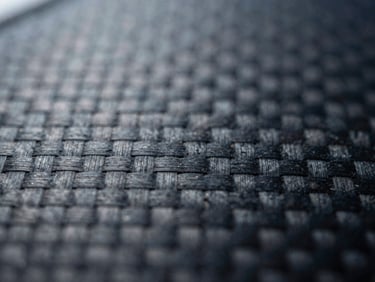 Macro shot of a damaged carbon fiber weave, high-contrast industrial lighting, desaturated steel and deep blue tones, 35mm