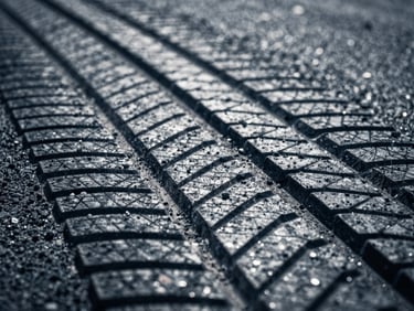 Tire tread marks on asphalt with sharp shadows, high-contrast industrial lighting, desaturated steel and deep blue tones, macro lens detail, 35mm