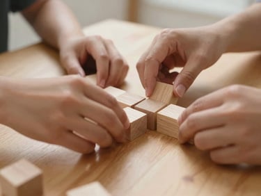 Close-up of hands collaborating on a shared wooden table, placing organic wooden blocks together, warm indoor light, shallow depth of field.