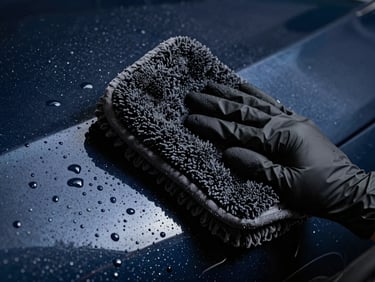 Macro shot of a black nitrile glove holding a thick plush microfiber wash mitt gliding over clean wet dark blue car paint with perfect water beading.