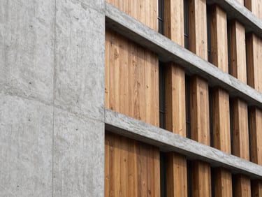 Close-up architectural detail of textured concrete and warm wood paneling on a modern office building, crisp natural shadows.