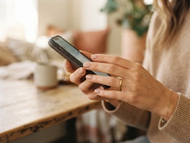 Close-up of a woman's hands gently holding a smartphone, soft natural daylight, shallow depth of field, neutral tones with blush accents, warm editorial fashion photography, 35mm