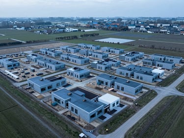 Aerial view of a new residential development site in a Dutch polder landscape, showing efficient land use and early-stage construction with foundations being laid, overcast daylight, cool blue and slate tones, sharp focus.