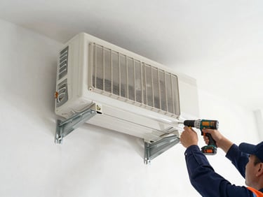 Wide overhead shot of a split-system air conditioner being mounted on an exterior wall, technician's hands securing the bracket with a drill, clean white concrete surface, even daylight