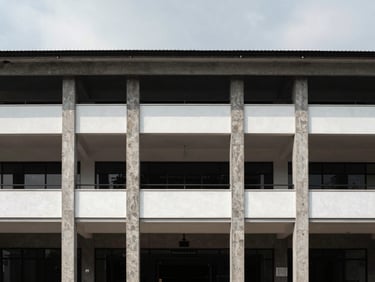 Wide daylight facade detail of a mixed-use commercial block in Bogor, exposed concrete columns framing retail frontage, signage bands empty, flat overcast sky above