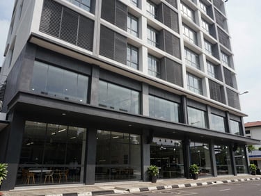 Wide daylight exterior of a mid-rise mixed-use building in Bekasi, ground-floor commercial units with glass shopfronts, upper residential floors with horizontal louvres, overcast natural light
