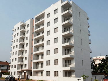 Wide shot of a modern residential apartment block in Visakhapatnam's MVP Colony, natural daylight, clean concrete facade with balconies, street-level context visible
