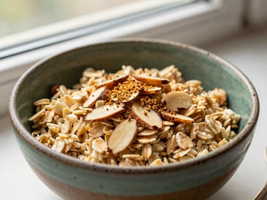 A rustic ceramic bowl of oatmeal topped with sliced almonds and a sprinkle of ground cardamom, warm window light