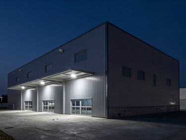 Architectural detail of a modern logistics warehouse exterior at night, sharp artificial lighting, dramatic shadows