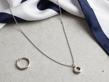 Macro flat-lay of elegant metallic jewelry and a silk scarf on a clean concrete surface, neutral daylight, sharp details