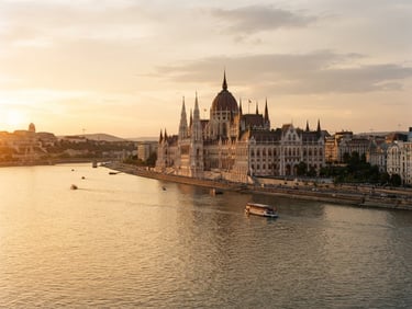Cinematic wide shot of Budapest parliament at golden hour, low sun casting warm amber light on the Danube river, 35mm film look, editorial framing.