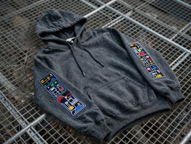 Landscape shot of a charcoal hoodie with embroidered modular patch bay diagrams on the sleeves, laid flat on a steel grid.