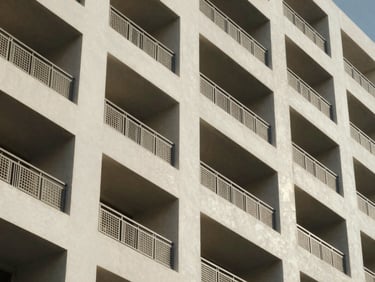 Close architectural detail of a mid-rise residential building façade in Abu Dhabi, north-facing diffused daylight, geometric balcony grilles casting shallow shadows on off-white render, upper floors receding slightly out of focus — no people, no staging