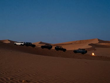 Anamorphic wide landscape shot of 4x4 vehicles silhouetted on massive Liwa sand dunes during deep blue hour