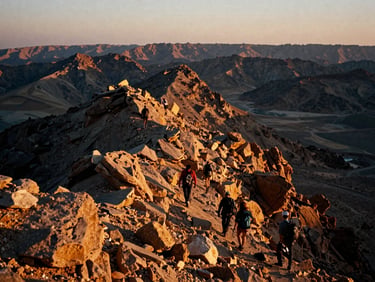 Candid 35mm film shot of hikers climbing a rugged mountain ridge in Jebel Jais during golden hour, deep shadows