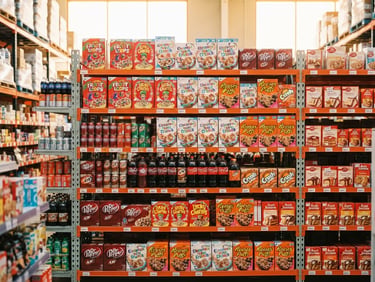 Straight-on medium shot of tidy, brightly lit Brisbane warehouse shelves stacked high with colorful authentic American cereals, sodas, and baking mixes, warm sunny daylight, vibrant saturated colors.