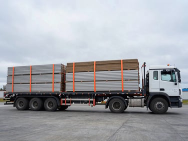Wide-angle shot of a flatbed truck loaded with construction materials, secured with safety orange straps, overcast northern sky, wide-angle lens.