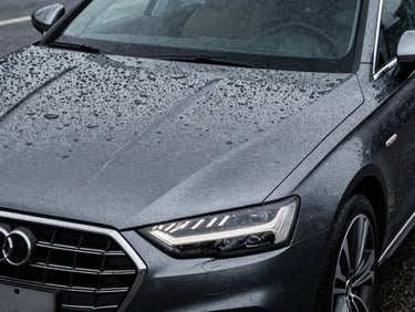 A clean luxury car driving through rain, water sheeting off the hood flawlessly, sharp focus on the hydrophobic surface, high-contrast studio lighting.