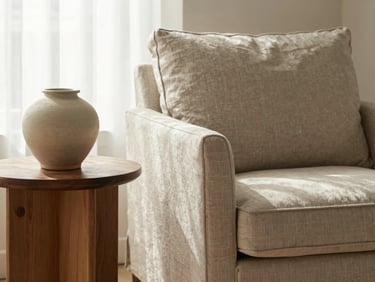 Close-up of styled interior staging, a linen armchair beside a wooden side table with a ceramic vase, soft morning light, editorial style.