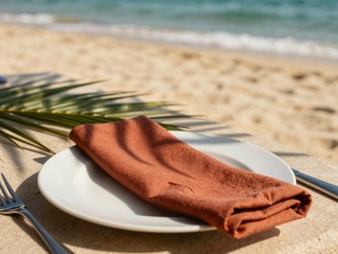 An elegant table setting on the sand, white plates, terracotta napkins, palm leaves casting soft dappled shadows, daytime ocean breeze, shallow depth of field, 35mm