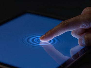 Macro studio shot of a finger touching a screen, creating subtle ripples of electric cobalt light representing tactile haptic feedback, dark background, cinematic lighting.