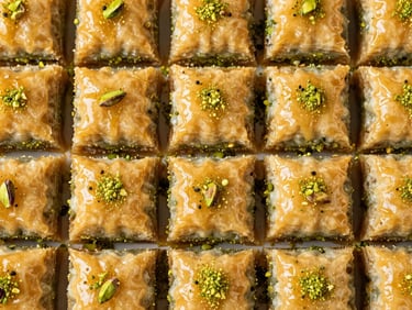 Overhead flat-lay of uniform rows of square pistachio baklava, glistening golden syrup, bright pistachio green dust, crisp natural side-lighting.