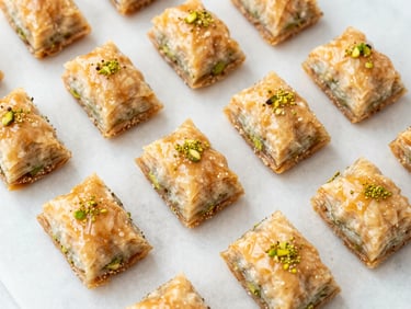 Overhead flat-lay of uniform baklava diamonds on a clean marble surface, bright natural side-light, warm honey and pistachio tones, shallow depth of field
