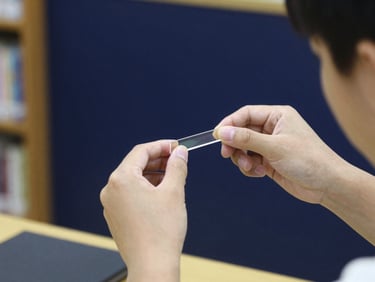A student adjusting a physics prism experiment, light refracting, dark navy background, crisp focus