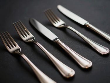 Close-up of polished silver cutlery arranged elegantly on a dark surface, subtle reflections, low-key lighting.