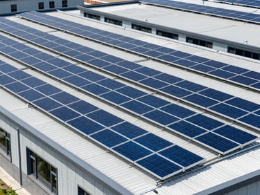 Wide environmental shot of commercial solar panels installed on a modern flat facility roof, clean architectural lines, crisp daylight, sharp geometric composition.