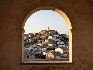 Wide environmental view looking through an open arched window of a traditional Sicilian house toward a sun-bleached hillside village in the distance, worn plaster wall framing the view, golden afternoon light, no people, eye-level perspective