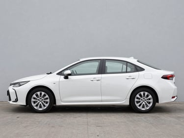 Full-side view of a white Toyota Corolla sedan parked on a clean neutral grey surface, natural overcast daylight, car centered in frame showing full profile, no people, studio-clean background
