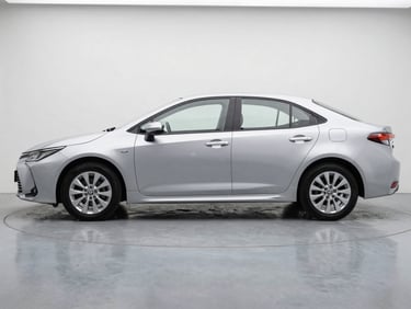 Side-on full view of a silver Toyota Corolla on a grey studio floor, natural overcast daylight, clean white background, showing true body finish