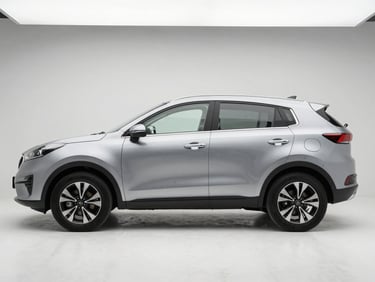 Side profile of a silver Kia Sportage on a white studio floor, diffused overhead light, full body visible with roof rack and factory trim intact