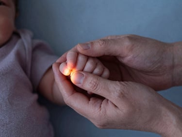 Close-up of an older sibling gently holding a newborn's tiny hand, soft warm lamp light, shallow depth of field, 35mm