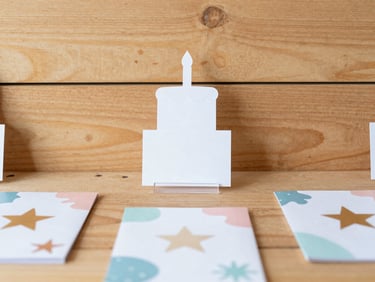 Styled flat lay of custom event decor including a cake topper, small acrylic sign, and personalized party favors, with stars and organic shapes, bright natural light, warm wood backdrop, scrapbook style