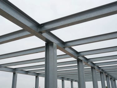 Environmental wide shot looking up at a steel structural framework mid-installation on a construction site, bolted connections and beam flanges visible in sharp detail, overcast on-site daylight, no workers in frame — scale communicated by the repeating column grid receding into the background