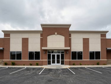 Straight-on elevation of a low-rise commercial building facade, brick and panel cladding freshly cleaned, flat overcast sky above, empty parking area below, no people or equipment