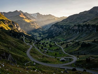 Wide-angle editorial shot of the Swiss Alps, a winding mountain road cutting through lush green valleys under crisp morning light.