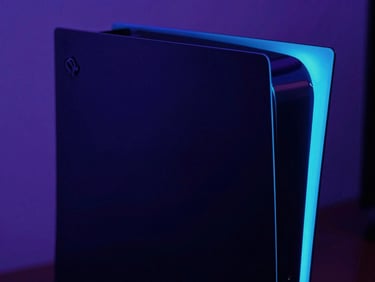 Sleek matte-black PlayStation console with sharp neon cyan LED strip glowing in a dark room, close-up geometric angle.