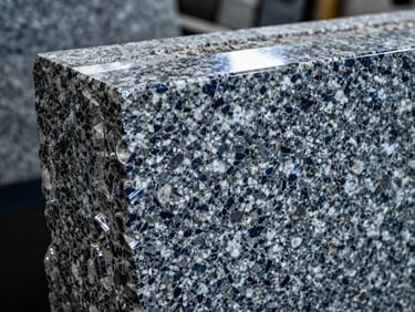 Close-up of a thick granite slab edge, polished to a gleam, under industrial workshop lighting, sharp focus on the stone's texture, deep navy and silver tones.