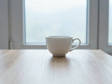 A quiet cup of tea sitting on a light oak table beside a window, soft morning window light, pale blue and warm white tones, clean minimalist composition, 35mm lens
