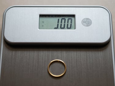 Extreme close-up of a certified digital scale display showing weight reading with small gold ring on the pan, bright even studio lighting, institutional framing