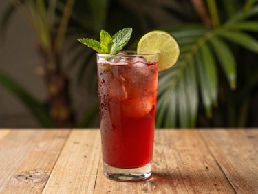 Glass of bright red hibiscus cooler with a slice of lime and mint, condensation on the glass, tropical background, natural light.