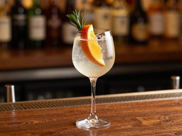 Elegant cocktail glass with a clear gin fizz, garnished with tropical fruit and a botanical sprig, soft lighting, upscale bar setting.