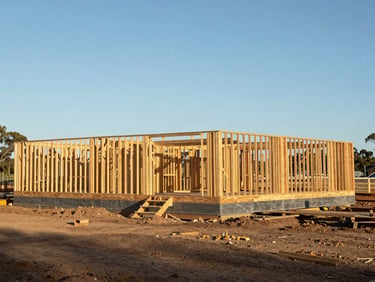 Wide environmental shot of an Australian residential construction site in progress, timber framing visible against a bright clear sky, no workers in frame, structured and ordered composition