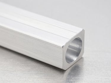 Macro close-up of a pristine CNC-milled aluminum component with sharp, clean edges, resting on a brushed steel surface under bright, high-key studio light, shallow depth of field.