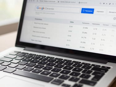 Close-up of a laptop keyboard with a Google Search Console performance report visible on the screen, impressions and click-through rate columns clearly legible, soft daylight from the left