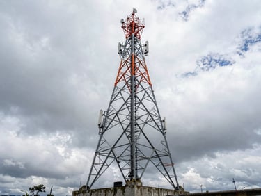 Industrial engineering photography, wide-angle shot of a massive steel telecom tower standing on a concrete foundation in the Colombian Andes, dramatic overcast sky, high-contrast steel tones.